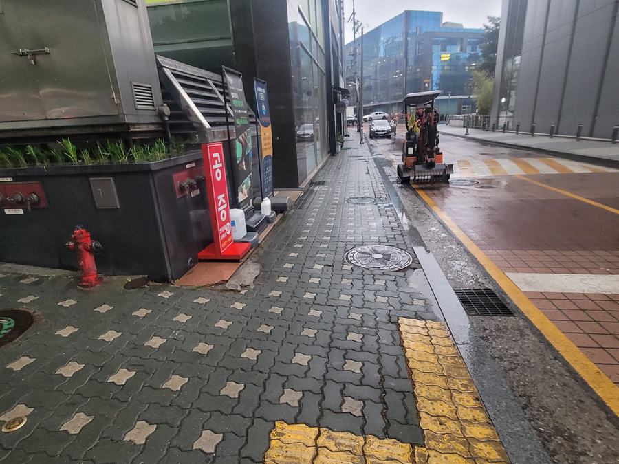 빗물 배수구와 완공된 보도블록, 굴착기가 있는 비 오는 날 현장